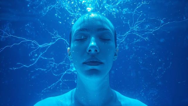 Serene woman floating underwater with closed eyes and ethereal hair filaments in blue