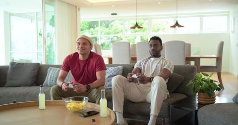 Two Friends Playing Console Games on Couch in Bright Modern Open-Plan Living Room
