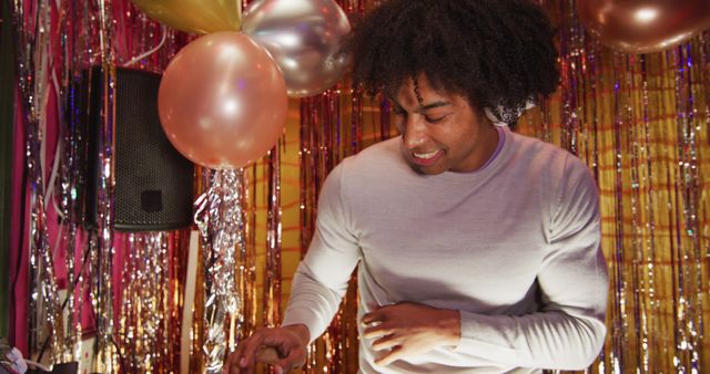 DJ with afro hair grooving under festive balloons and gold tinsel creates energetic and lively atmosphere perfect for party promotions, music event advertisements, and nightlife marketing. Ideal for showcasing fun and entertainment at celebrations.