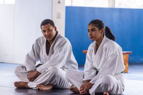 Martial arts partners sitting on dojo mat in white judogi