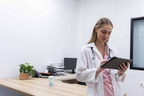 Female physician using tablet in modern medical office with stethoscope and workspace