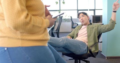 Male colleague leaning back and gesturing while coworker using phone in open-plan office
