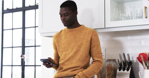 Man in Modern Kitchen Checking Smartphone Beside Jar of Pasta