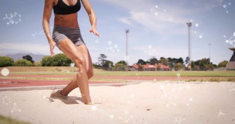 Female long jump athlete landing in sand pit on outdoor track showing power and speed