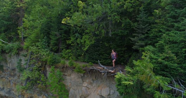 A young Caucasian woman stands on the edge of a cliff surrounded by lush greenery, with copy space - Download Free Stock Photos Pikwizard.com