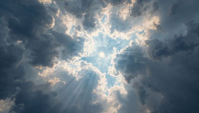 Sunburst piercing layered clouds casting dramatic crepuscular rays across deep blue sky