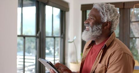Senior man engaged with tablet by large modern windows