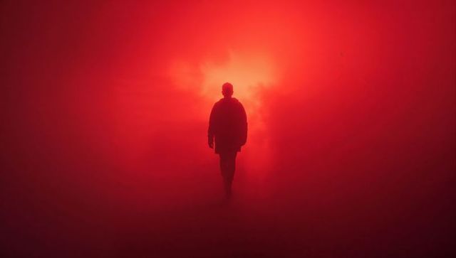 Silhouetted Man Walks Toward Red Light in Foggy Atmosphere