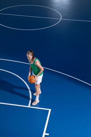 Female basketball player dribbling on blue court in action scene