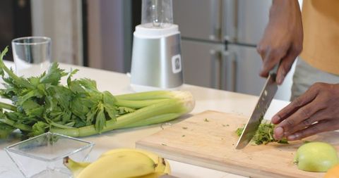 African American man chopping herbs on wooden board in kitchen preparing healthy drink
