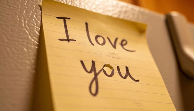 Handwritten i love you sticky note sticking to fridge surface showing small puncture