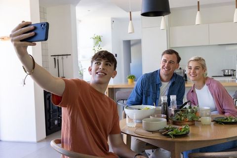 Young man taking selfie with friends during casual kitchen lunch in modern home