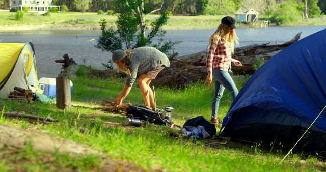 Two friends setting up tent by riverside in forest, enjoying nature and preparing camping site. Ideal for promoting outdoor activities, camping gear, teamwork, summer vacations, and nature exploration.