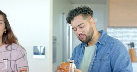 Couple enjoying casual meal at modern kitchen counter eating burger and sipping drink