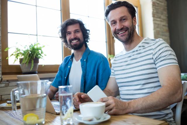 Portrait of two smiling men sitting at table in coffee shop