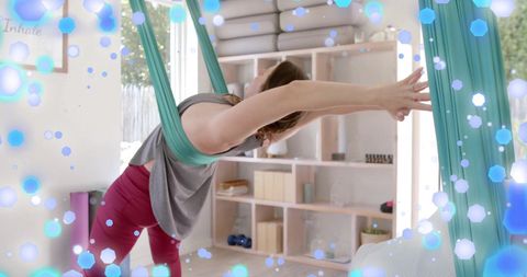 Caucasian Woman Practicing Aerial Yoga with Digital Light Effects