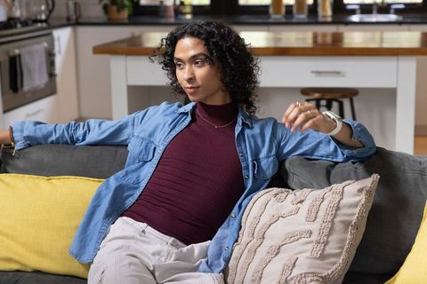 Relaxed non-binary person reclining on sofa in modern minimalist open-plan living space