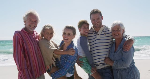 Multigenerational family including grandparents, parents, and children standing together on beach with ocean behind them. Ideal for use in advertisements promoting family vacations, travel destinations, or togetherness and bonding. Perfect for illustrating concepts of family love, summer holidays, and relaxation.
