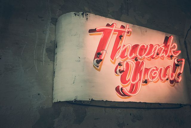 Neon Thank You sign glowing against worn wall. Perfect for articles on retro decor, urban aesthetics, and gratitude. May be used for branding and marketing of creative and industrial-related products.