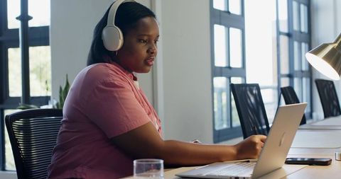 Black woman typing on laptop with headphones in contemporary coworking hub