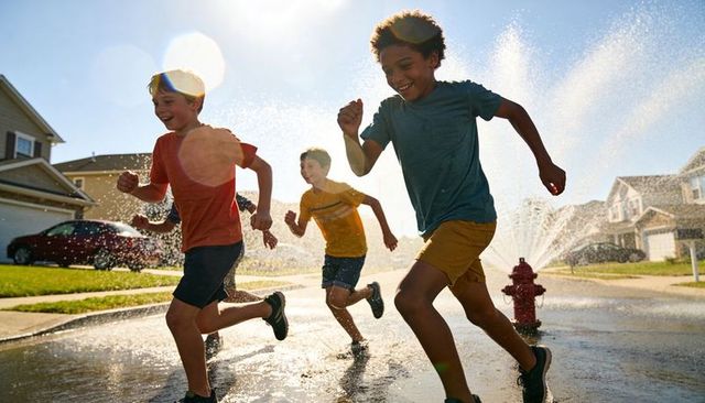 Three boys running and splashing through fire hydrant spray on sunny suburban street