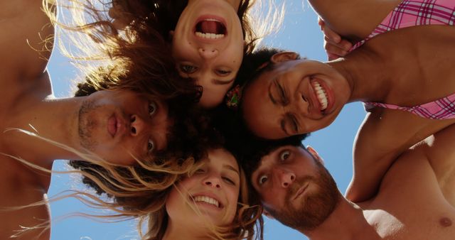 Low angle portrait of happy diverse friends making funny faces and embracing against sunny blue sky. Summer, vacations, friendship, fun, togetherness and relaxation, unaltered.