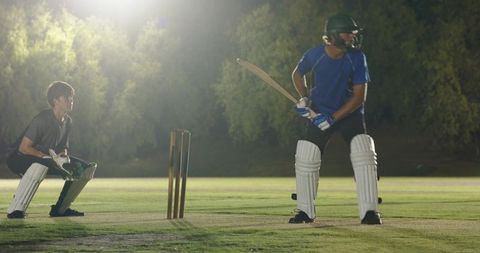 Night cricket batsman preparing to strike under floodlights with wicketkeeper crouching