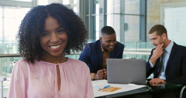 Confident Businesswoman Smiling in Modern Office with Colleagues Working in Background - Download Free Stock Images Pikwizard.com