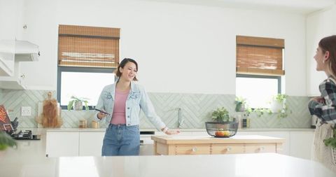 Sunlit modern kitchen friends chatting at wooden island with smartphone beside fruit bowl