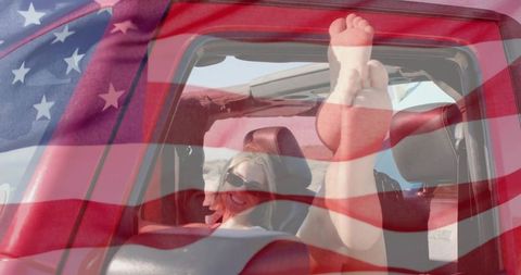 Carefree woman relaxing in red jeep convertible with feet up and american flag overlay