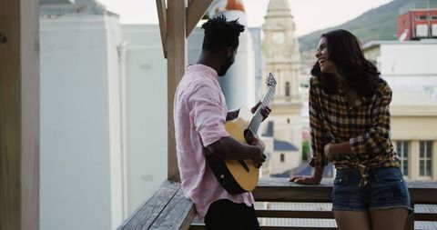 Joyful Friends Sharing Music on Rooftop During Sunset