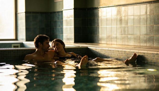 Sunlit romantic couple relaxing in indoor mosaic pool, intimate spa escape at dusk