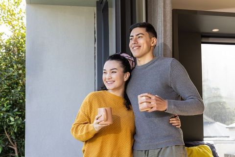 Young couple enjoying morning coffee on balcony, cozy sweaters and sunlit garden view