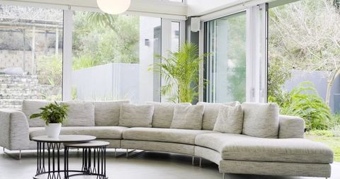 Sunlit curved gray sectional sofa in minimalist open-plan living room with garden view