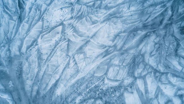 Aerial abstract of blue glacier ice revealing jagged fissures and crystalline ridges