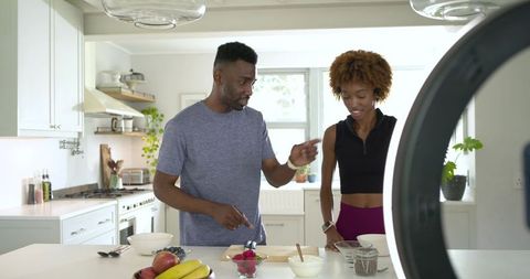 Diverse couple preparing healthy breakfast bowls at sunlit modern kitchen island