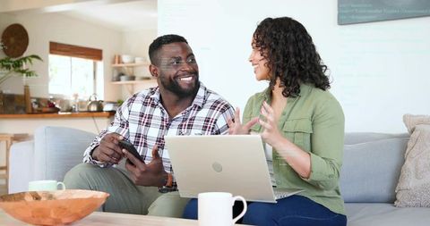 Smiling couple chatting and working on laptop and smartphone in cozy modern living room
