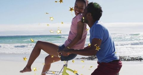 Joyful Couple Biking on Beach Amidst Sparkling Confetti