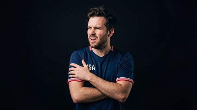 Confused athlete touching sore shoulder while crossing arms wearing navy usa sports jersey