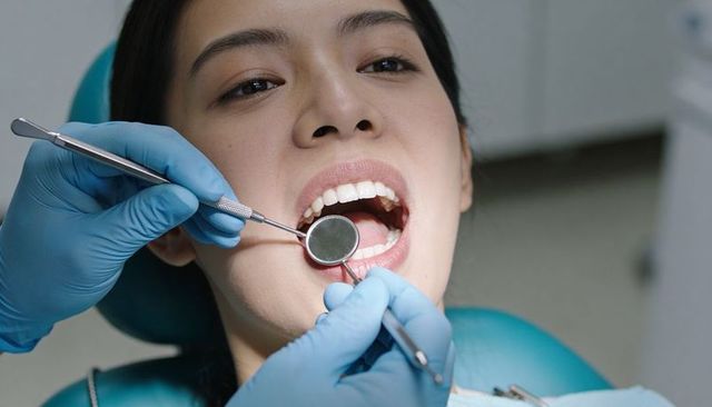 Close-up dentist examining adult asian woman teeth with mirror and probe in dental clinic