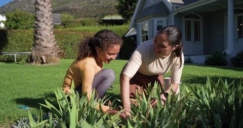 Mother and daughter gardening together in sunny front yard with green lawn
