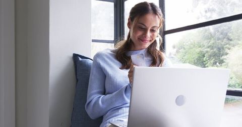 Woman Enjoying Work from Home by Window on Laptop
