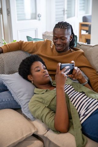 African American Couple Relaxing on Sofa with Smartphone