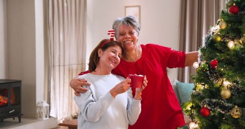 Senior mother and daughter enjoying christmas by tree with hot beverage
