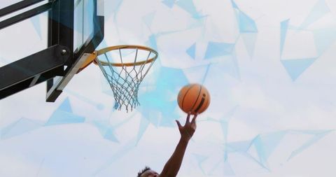 Male basketball player reaching rim midair layup on outdoor court against blue sky
