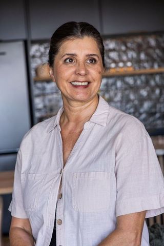 Mature woman smiling, looking right, standing in modern kitchen with stainless fridge