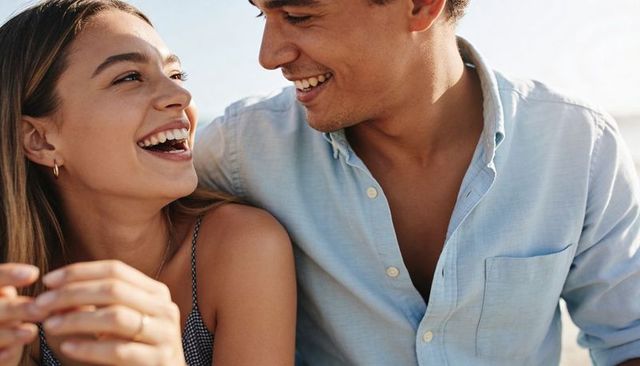 Sunlit smiling couple sharing laugh on beach closeup romantic summer golden hour portrait