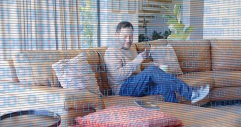 Mature Asian Man Relaxing on Sofa Using Smartphone with Digital Binary Overlay