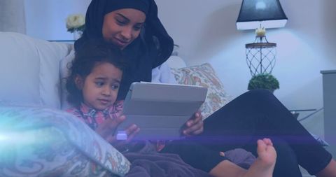 Smiling Biracial Mother in Hijab with Daughter Using Tablet at Home
