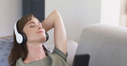 Caucasian Woman Relaxing on Couch Listening to Music on Headphones